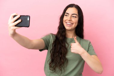 Pembe arka planda izole edilmiş beyaz bir kadın cep telefonuyla selfie çekiyor.
