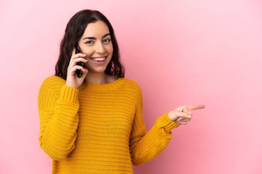 Pembe arka planda izole edilmiş cep telefonu kullanan beyaz bir kadın.