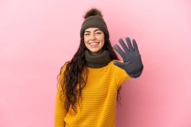 Mor arka planda izole edilmiş kışlık şapkalı beyaz kız parmaklarıyla beşi sayıyor.