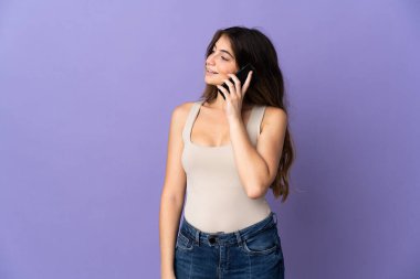 Mor arka planda izole edilmiş genç, beyaz bir kadın cep telefonuyla sohbet ediyor.