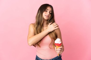 Kornet dondurması olan beyaz bir kadın pembe arka planda izole edilmiş ve omuz ağrısı çekiyor.
