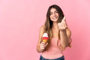 Pembe arka planda izole edilmiş kornet dondurmalı beyaz bir kadın para hareketi yapıyor.