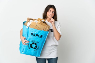 Elinde kağıt dolu bir geri dönüşüm çantası olan genç bir kadın beyaz arka planda izole edilmiş bir şekilde duruyor. Şüpheleri ve düşünceleri var.