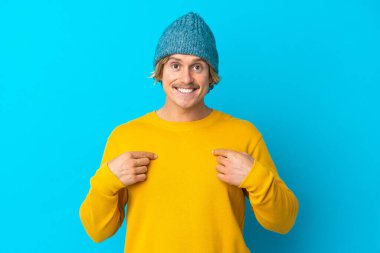 Yakışıklı sarışın adam, mavi arka planda mahsur kalmış, şaşırmış bir yüz ifadesi var.