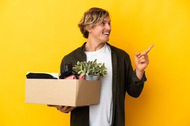 Sarışın adam sarı arka planda izole edilmiş şeylerle dolu bir kutuyu kaldırırken hareket ediyor. Çözümü fark etmek için parmağını kaldırıyor.