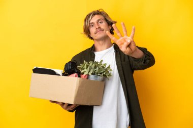 Sarı arka planda izole edilmiş şeylerle dolu bir kutuyu kaldırırken sarışın adam hamle yapıyor mutlu ve parmakları olan dört kişi sayıyor.