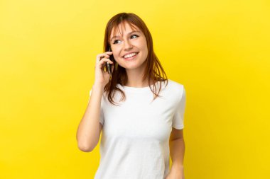 Sarı arka planda izole edilmiş kızıl saçlı bir kız cep telefonuyla sohbet ediyor.