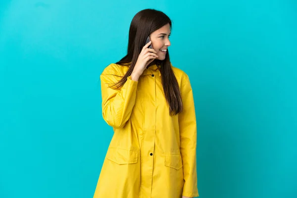 ティーンブラジルの女の子身に着けていますレインプルーフコート上の隔離された青の背景に誰かと携帯電話との会話を保ちます — ストック写真