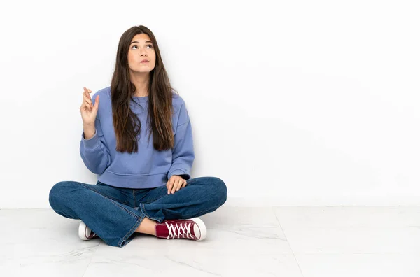 Young woman sitting on the floor with fingers crossing and wishing the best