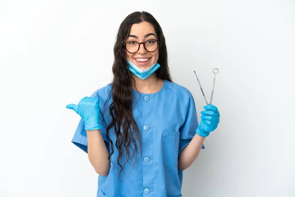 Młoda Kobieta Dentysta Trzyma Narzędzia Izolowane Białym Tle Wskazując Bok — Zdjęcie stockowe