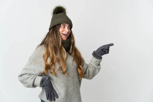 年轻的高加索女人 头戴冬季帽 白色背景隔离 手指指向侧面 展示了一种产品 — 图库照片
