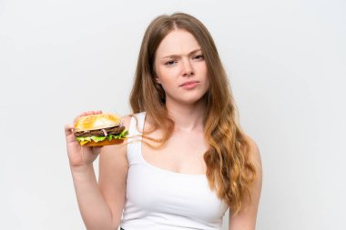 Genç, güzel bir kadın, elinde hamburgerle, üzgün bir ifadeyle beyaz arka planda.