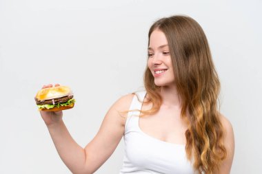 Genç, güzel bir kadın elinde hamburgerle beyaz arka planda mutlu bir ifadeyle.