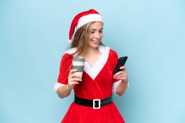 Anne-Baba gibi giyinmiş genç sarışın kadın mavi arka planda izole edilmiş. Elinde kahve ve cep telefonu var.