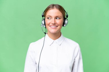 Tele pazarlamacı beyaz kadın, izole edilmiş arka planda mutlu bir ifadeyle kulaklıkla çalışıyor.