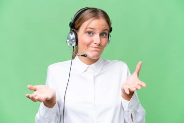 Tele pazarlamacı beyaz kadın izole edilmiş bir arka planda kulaklıkla çalışıyor. Omuzlarını kaldırırken şüpheli hareketler yapıyor.