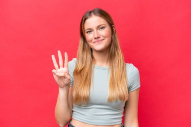 Kırmızı arka planda izole edilmiş güzel bir kadın mutlu ve parmaklarıyla üçe kadar sayıyor.