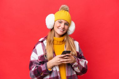 Kırmızı arka planda izole edilmiş kışlık kuklalar takan güzel bir kadın cep telefonuyla mesaj yolluyor.