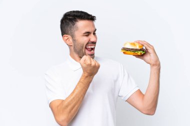 Genç, yakışıklı, beyaz bir adam, arka planda bir hamburgerle zaferi kutluyor.