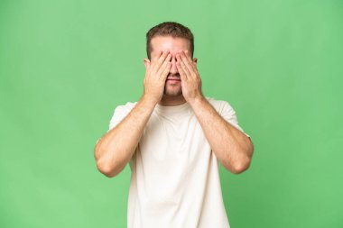 Yeşil krom arka planda izole edilmiş yakışıklı beyaz adam gözleri elleriyle kaplıyor.