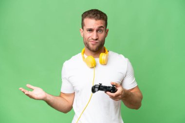 Yeşil krom arka planda izole edilmiş bir video oyunu kontrolörüyle oynayan yakışıklı genç adam, omuzlarını kaldırırken şüpheli hareketler yapıyor.