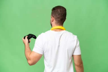 Arka planda yeşil renkli arka planda izole edilmiş bir video oyunu kontrolörüyle oynayan genç yakışıklı adam.