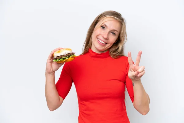 Młoda Blondynka Trzyma Hamburgera Białym Tle Uśmiechając Się Pokazując Znak — Zdjęcie stockowe
