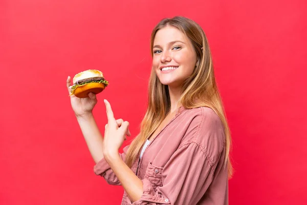Молода Біла Жінка Тримає Бургер Ізольовано Червоному Тлі Вказує Нього — стокове фото