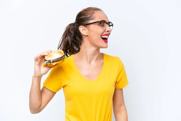 Młoda Kaukaska Kobieta Trzyma Hamburgera Odizolowanego Białym Tle Śmiejąc Się — Zdjęcie stockowe