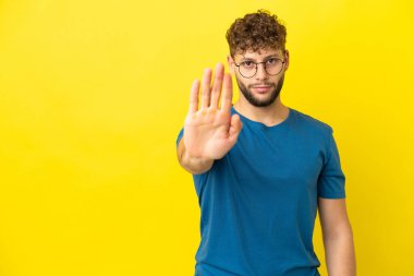 Sarı arka planda izole edilmiş yakışıklı beyaz adam dur hareketi yapıyor.