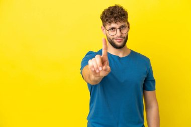 Sarı arka planda izole edilmiş yakışıklı beyaz adam parmağını kaldırıyor.