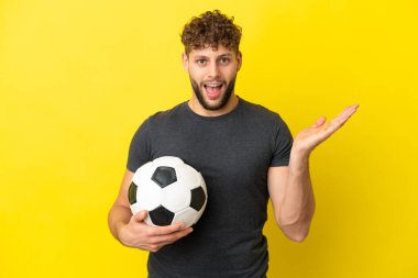Yakışıklı genç futbolcu, sarı arka planda izole edilmiş, şok olmuş bir yüz ifadesi var.