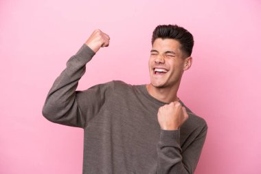 Pembe arka planda izole edilmiş genç beyaz bir adam zaferi kutluyor.