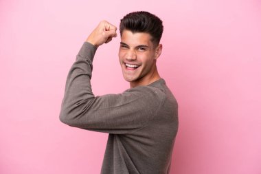 Pembe arka planda izole edilmiş genç beyaz adam güçlü bir jest yapıyor.