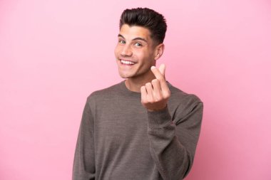 Pembe arka planda izole genç beyaz adam para hareketi yapıyor.