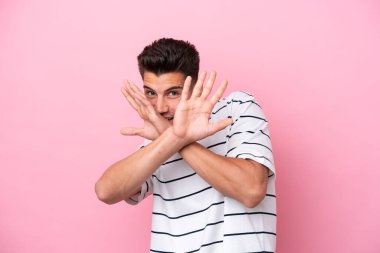 Pembe arka planda izole edilmiş genç beyaz adam sinirden ellerini öne uzatıyor.