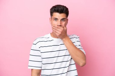 Pembe arka planda izole edilmiş, ağzı elle kaplanmış genç beyaz bir adam.