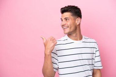 Pembe arka planda izole edilmiş genç beyaz adam bir ürünü sunmak için kenarı işaret ediyor.
