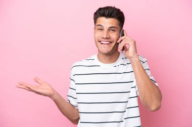 Pembe arka planda izole edilmiş genç beyaz bir adam cep telefonuyla sohbet ediyor.