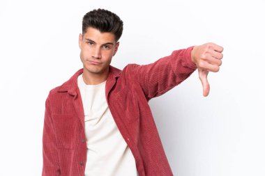 Beyaz arka planda izole genç beyaz adam olumsuz ifade ile baş parmağını göstermektedir