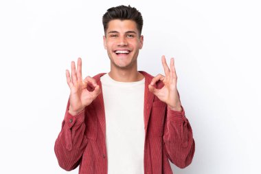 Beyaz arka planda izole edilmiş genç beyaz bir adam iki eliyle tamam işareti gösteriyor.