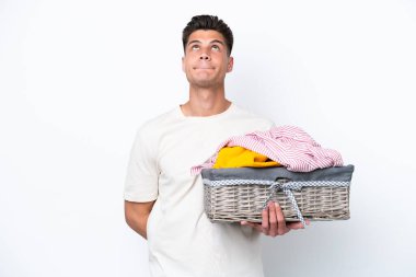 Beyaz arka planda çamaşır sepetini tutan genç beyaz bir adam var.