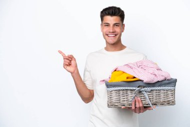 Young caucasian man holding laundry basket isolated on white background pointing to the side to present a product