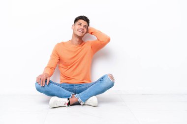 Genç bir adam beyaz arka planda izole bir şekilde yerde oturuyor.