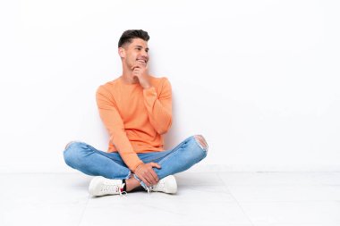 Genç adam beyaz arka planda izole bir şekilde yerde oturuyor.