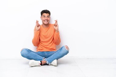 Genç adam beyaz arka planda izole bir şekilde yerde oturuyor.