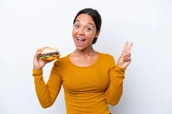 Młoda Latynoska Kobieta Trzyma Hamburgera Odizolowanego Białym Tle Uśmiechając Się — Zdjęcie stockowe