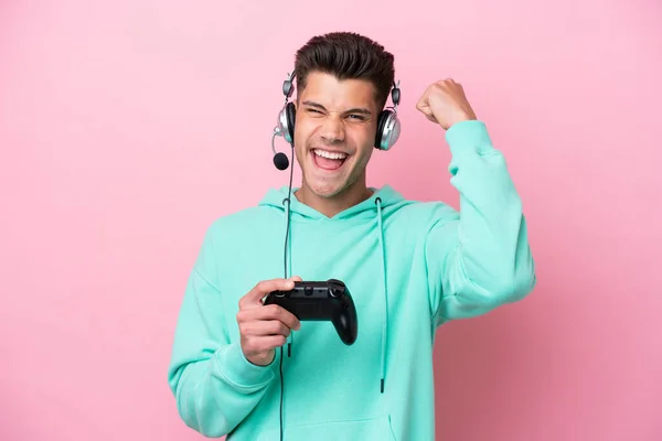 若いですハンサムな白人男性遊びますとともにAビデオゲームコントローラ孤立ピンクの背景に祝う勝利 — ストック写真
