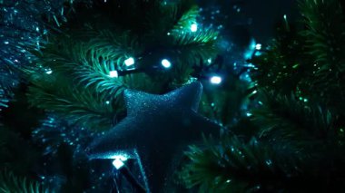 Vertical loop abstract background macro video of a silver Christmas tree star decoration on a green tree with blue and green repetitive fairy lights flashing and fading through each other.