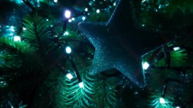 A close up looped horizontal shot of a silver star shaped decoration on an artificial Christmas tree with colour changing flashing twinkling LED fairy lights.